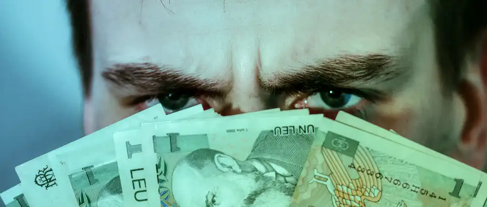 Angry man peeping over bills of money.