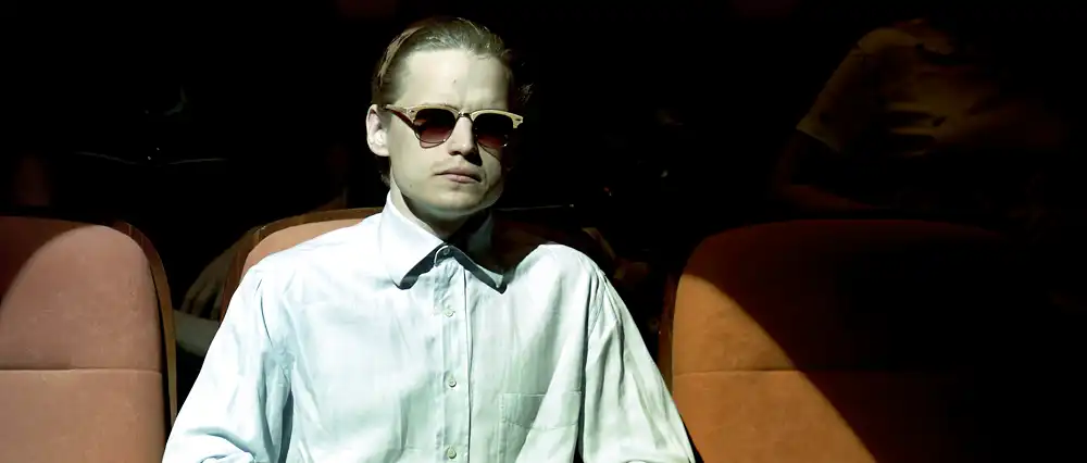 Man under spotlight seated in a row of chairs.