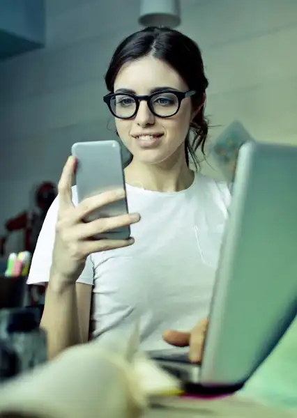 Woman looking at smartphone while at the laptop. 